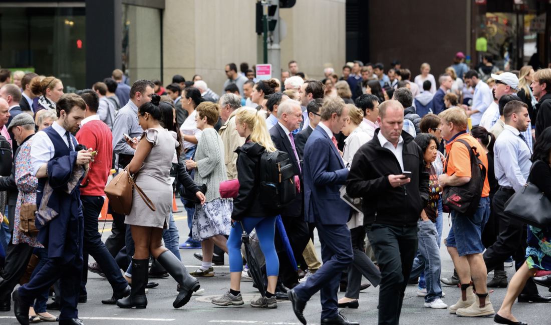 A crowded city crossing, most of the faces down over phones