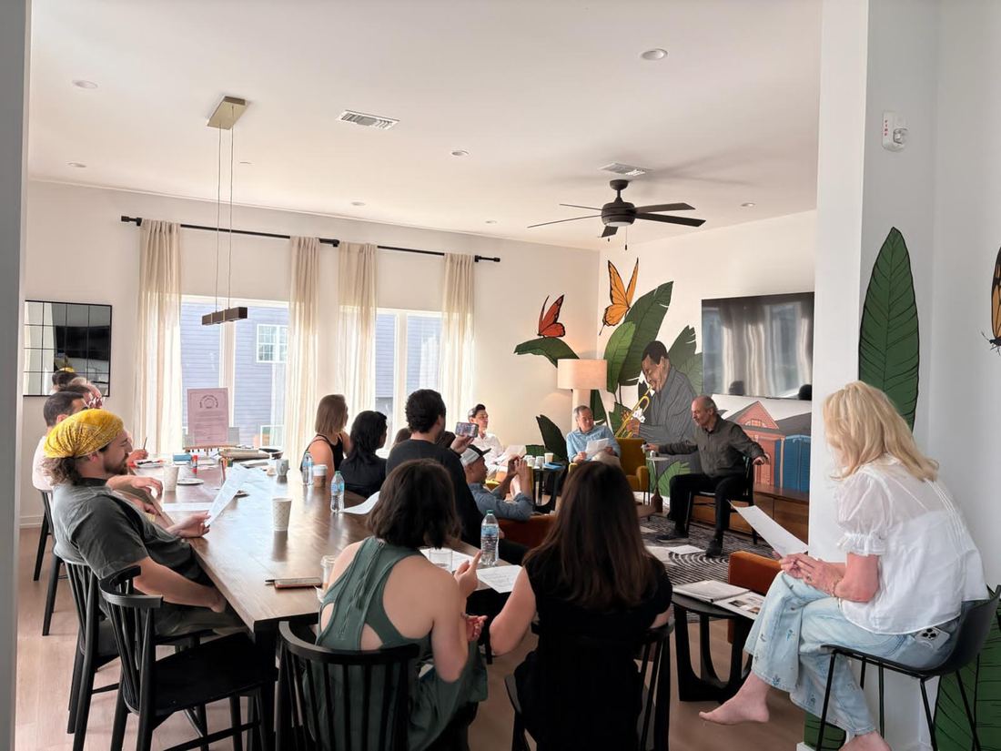 A group in a New Orleans living space, a man up front with his arms wide, telling a story
