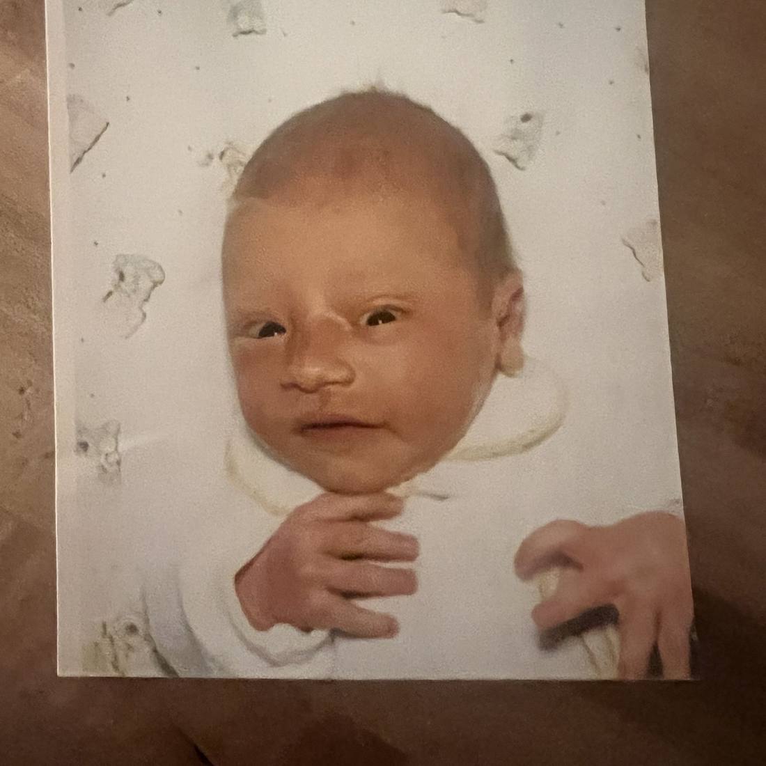 A newborn, eyes barely open, fingers crooked at the chin