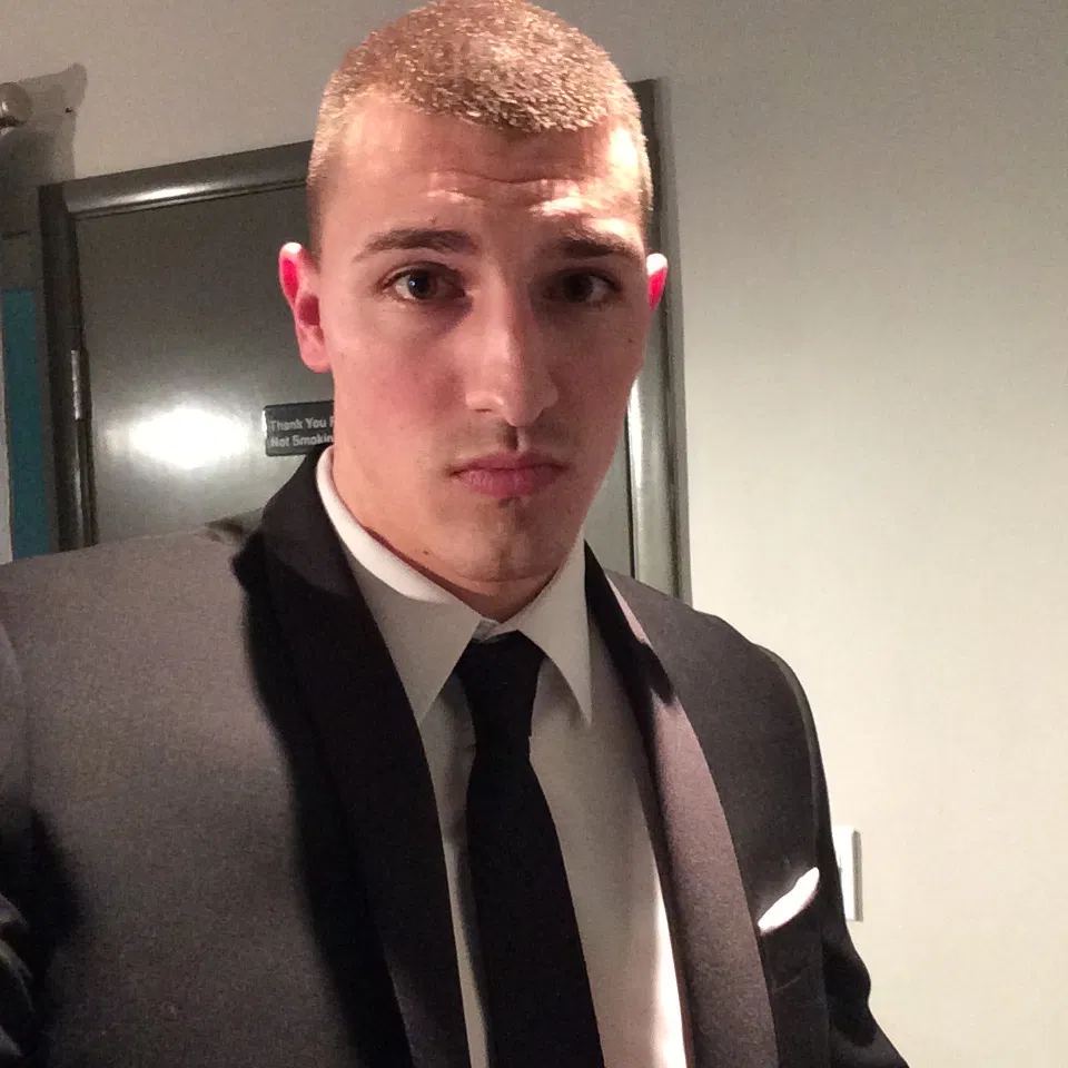 A younger me in a suit and tie, buzzcut bleached blond, unsmiling