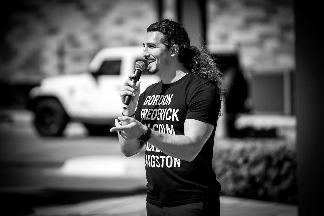 Mid-sentence with a microphone outdoors, in black and white